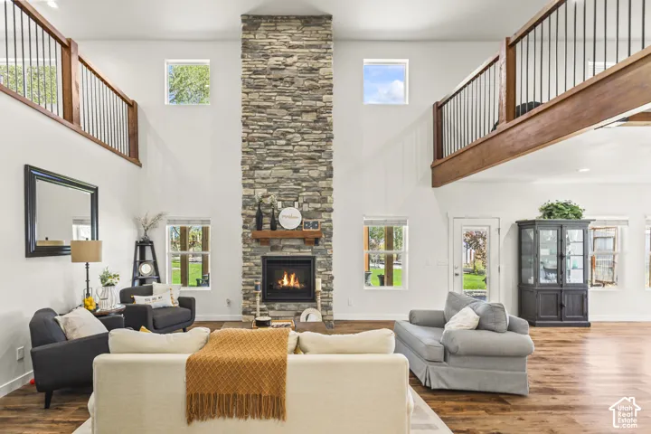 Double-height ceiling featuring a full-height stacked stone fireplace, wood-finish flooring, and dual mezzanine-style walkways with wood and metal railings