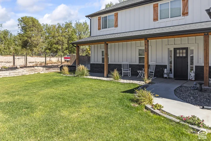 Two-story farmhouse-style exterior featuring vertical board-and-batten siding, dark stone veneer skirting, wood-finish shutters, a full-length covered porch with timber support beams, and a concrete walkway