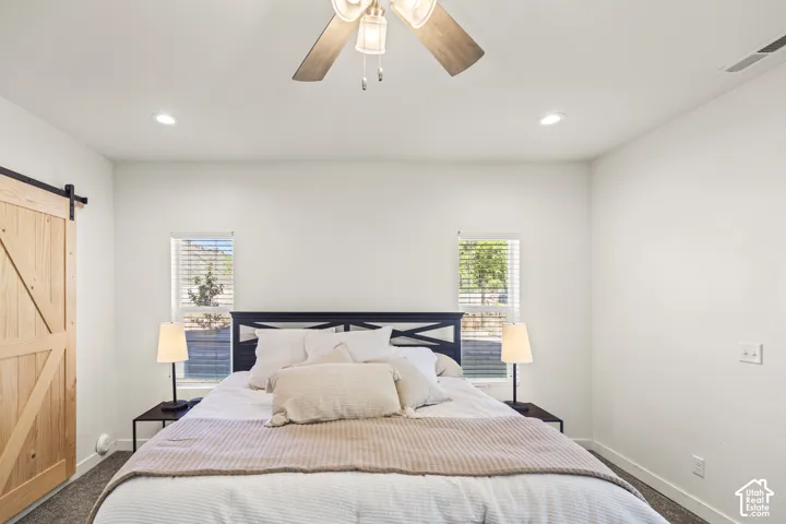 Neutral room featuring a ceiling fan with integrated lighting, dual windows with blinds, and a wood-finish sliding barn door