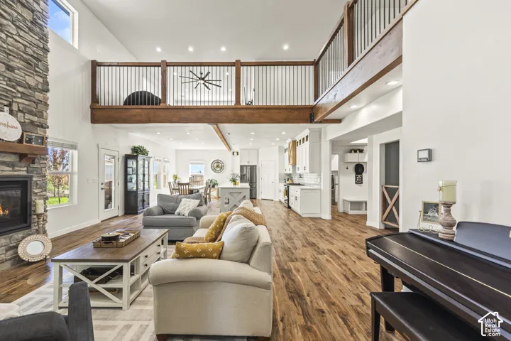 Open-concept living space featuring high ceilings, floor-to-ceiling stone-surround fireplace, wood-finish flooring, and an elevated wooden mezzanine with metal balusters