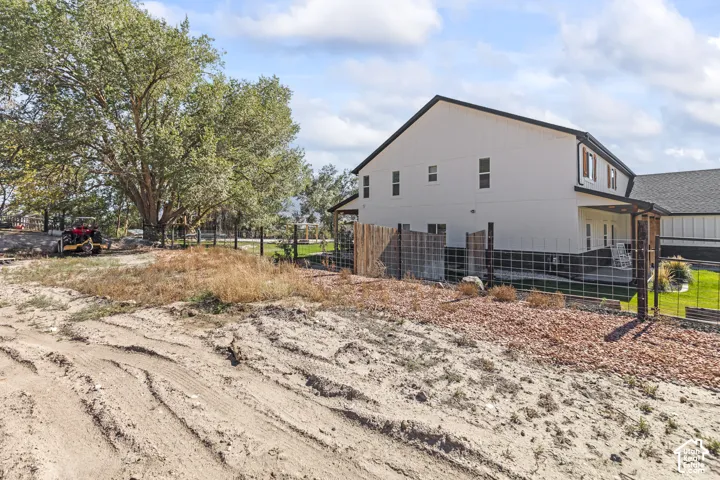 Two-story exterior featuring light-toned vertical siding, dark trim, a covered side patio, and wire perimeter fencing