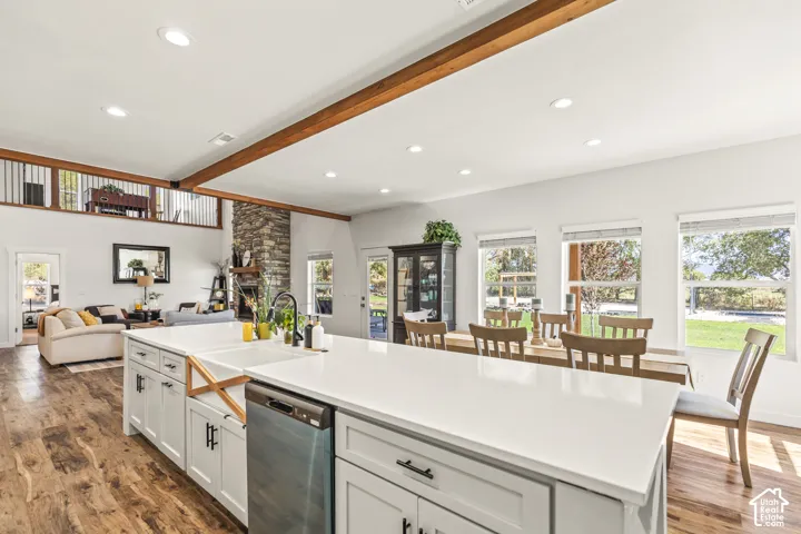 Kitchen featuring a large center island with a white surface, farmhouse apron-front sink, wood-finish flooring, exposed ceiling beams, and a floor-to-ceiling stone fireplace