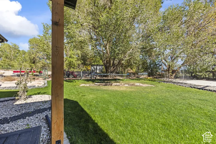Backyard featuring a grass lawn, decorative stone ground cover, a wood-finish support post, and mature trees