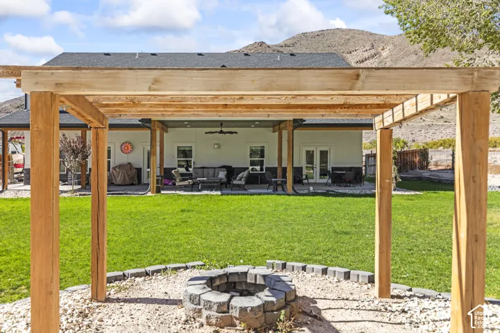 Backyard featuring a timber-frame pergola, a circular stone fire pit, a concrete patio, and a manicured lawn set against a mountain backdrop