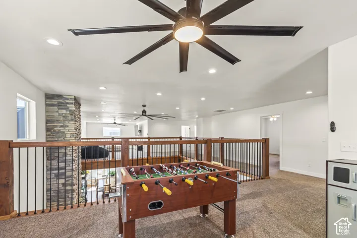 Open-concept interior featuring recessed lighting, large multi-blade ceiling fans, a full-height stone masonry wall, and wooden railing with metal balusters