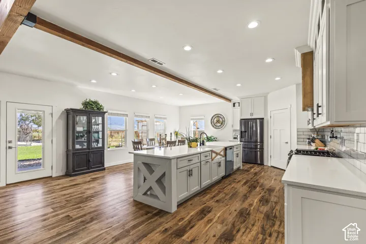 Kitchen featuring wood-finish flooring, a central island with X-frame detailing, quartz countertops, subway tile backsplash, and a wooden ceiling beam
