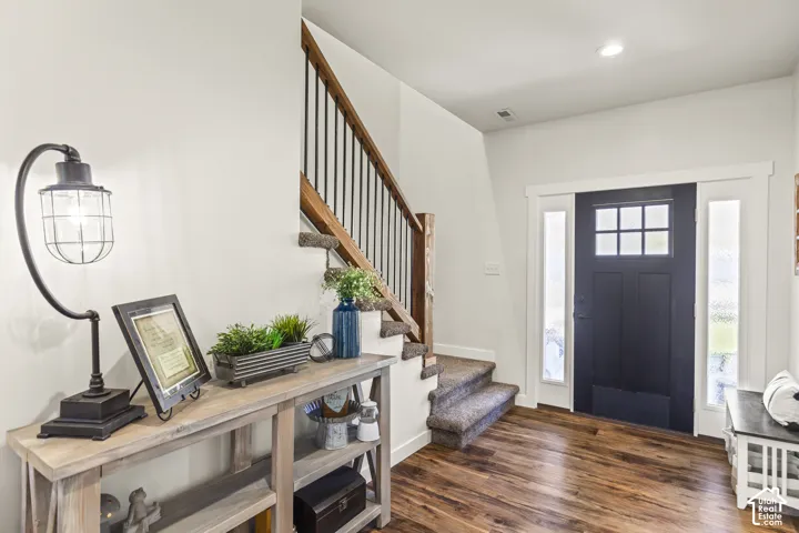 Entryway featuring wood-finish flooring, a solid-core front door with multi-pane glass inlay, side light panels, and a staircase with a wood handrail and vertical metal balusters