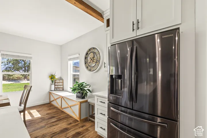 Kitchen featuring white shaker-style cabinetry, wood-finish flooring, built-in bench seating with lattice detail, a stainless steel refrigerator, and an exposed wooden ceiling beam