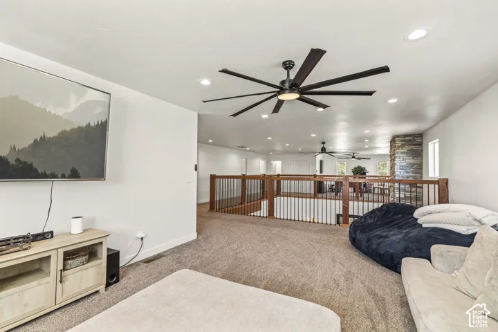 Open-concept area featuring recessed lighting, a multi-blade ceiling fan, stacked stone pillar accents, and a staircase gallery with wood-topped railings and metal spindles