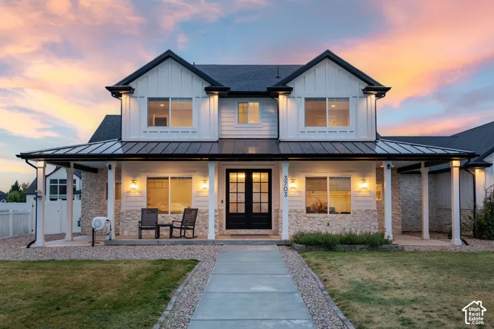 Two-story farmhouse exterior featuring a metal roof, vertical board-and-batten siding, stone masonry accents, and a covered front porch with square columns