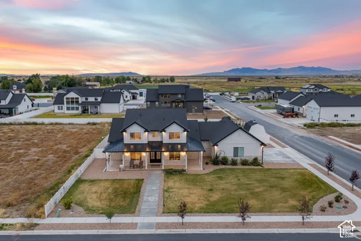Two-story farmhouse-style residence featuring a metal roof, stone and board-and-batten siding, a covered front porch, and an expansive lawn