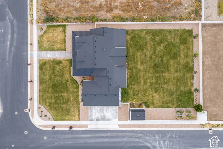 Aerial perspective of a corner lot featuring a dark-toned asphalt shingle roof, concrete driveway, expansive sodded grounds, and a detached structure