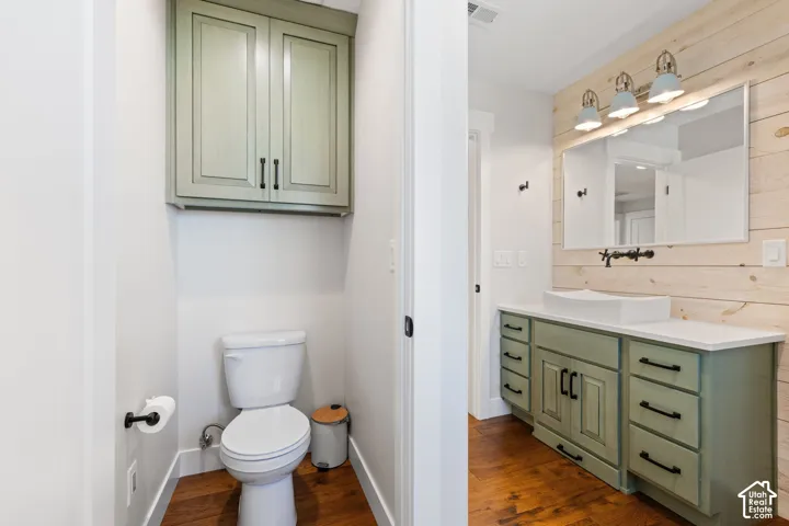 Second floor bathroom featuring hardwood flooring, a wall-mounted vessel sink, sage green built-in cabinetry with matte black hardware, and wood-plank accent wall