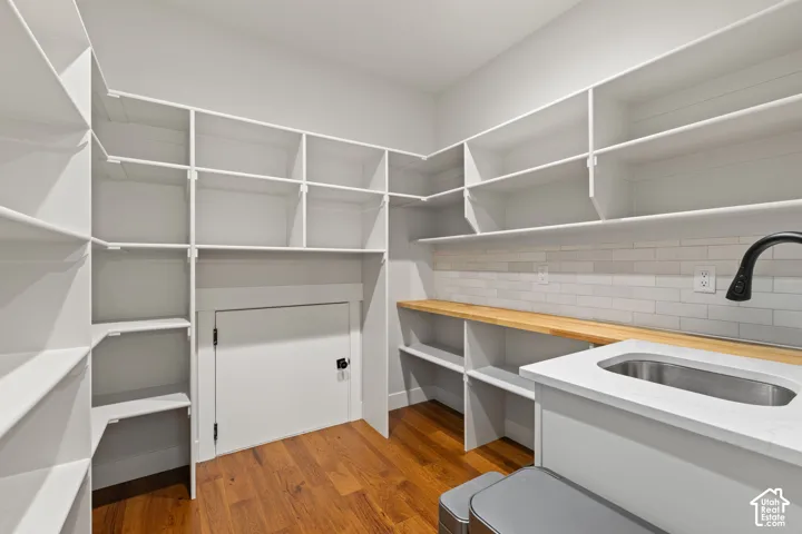 Walk-in storage space featuring custom white shelving, hardwood flooring, butcher block countertop, undermount sink with matte black faucet, and horizontal tile backsplash