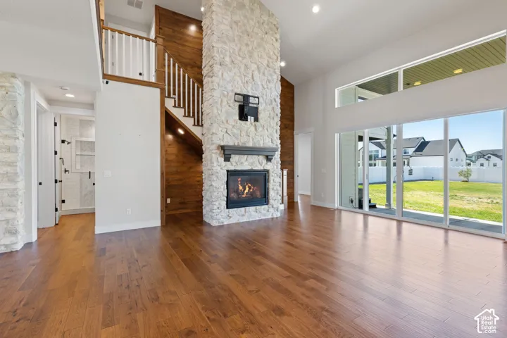 Double-height ceilings, floor-to-ceiling stone fireplace, hardwood flooring, wood paneling accent wall, and expansive sliding glass doors