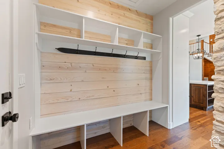 Built-in storage bench featuring light-toned wood-plank wall paneling, white open shelving, a matte black metal coat rack, and hardwood flooring
