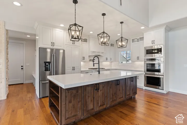 Kitchen featuring white shaker-style cabinetry, a contrasting wood-finish kitchen island with a light quartz countertop, stainless steel double wall ovens, three geometric pendant lights, and hardwood flooring