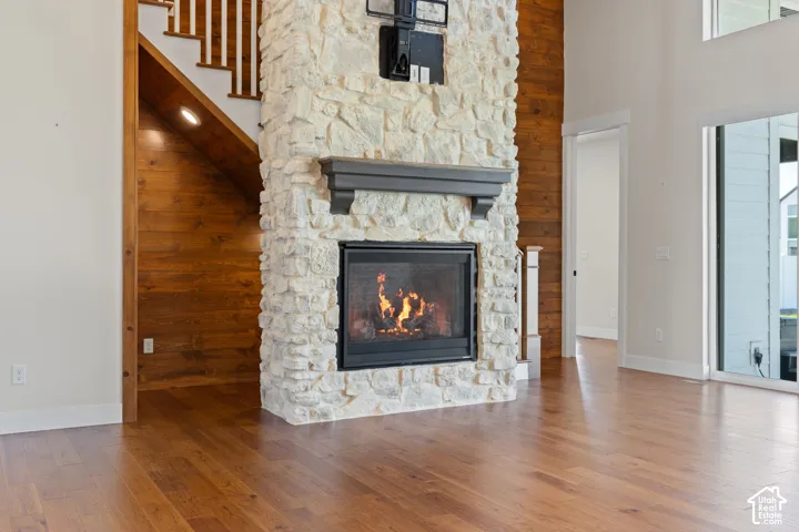 Floor-to-ceiling stone fireplace featuring a prominent mantel and hearth, hardwood flooring, wood-plank accent wall, and staircase with painted railing