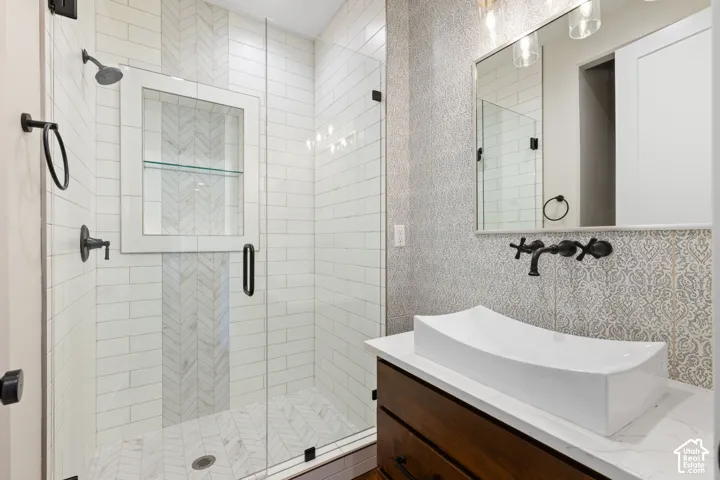 Main floor bathroom featuring walk-in glass-enclosed shower with herringbone tile detailing, built-in shelving niche, wall-mounted vessel sink, and matte black plumbing fixtures