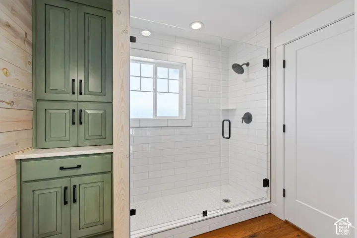 Walk-in shower featuring a frameless glass door, white subway tile surround, matte black fixtures, and recessed lighting, complemented by built-in green cabinetry with matte black hardware and hardwood