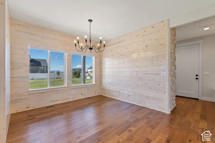 Dedicated dining space featuring horizontal wood-plank wall treatments, hardwood flooring, a multi-arm metal chandelier, large windows with exterior surroundings, and a natural stone accent wall