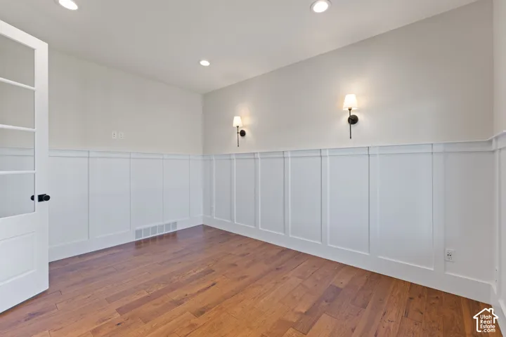 Room featuring hardwood flooring, white board-and-batten wall detailing, recessed lighting, and wall-mounted sconces, accessible via a multi-lite French door