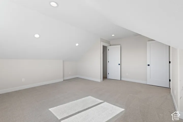 Neutral-toned bedroom featuring slanted ceilings, recessed lighting, wall-to-wall carpeting, and two interior doors with matte black hardware