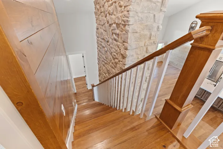 Staircase featuring hardwood flooring, horizontal wood wall paneling, a floor-to-ceiling natural stone fireplace, and a wooden handrail with white balusters