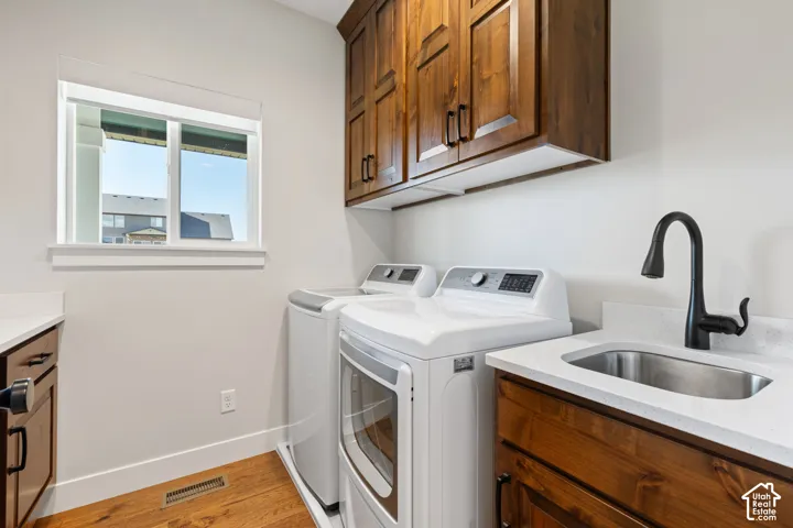 Laundry room featuring stained wood cabinetry, white quartz countertops, a drop-in stainless steel sink with a matte black faucet, and hardwood flooring