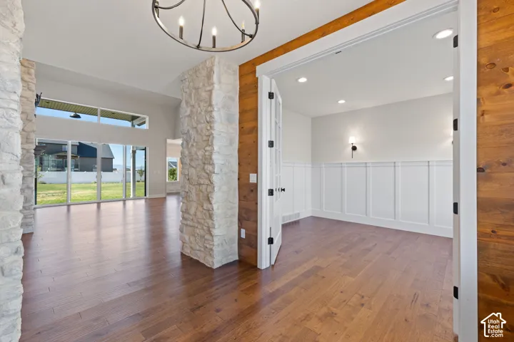 Open floor plan featuring hardwood flooring, floor-to-ceiling stone pillar accents, wood-plank wall paneling, and a room enclosed by French doors with white wainscoting