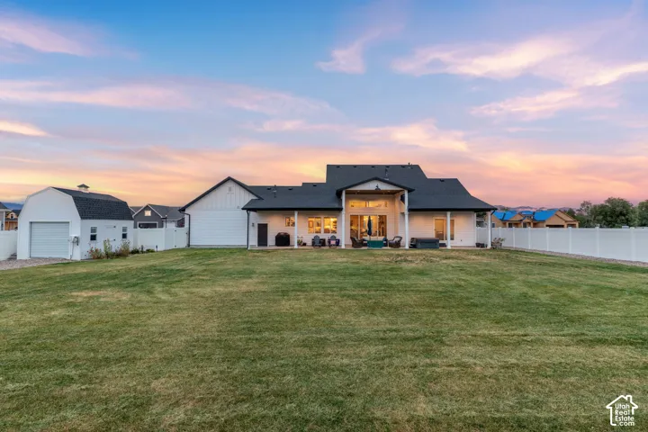 Expansive backyard featuring a manicured lawn, detached barn-style garage, covered patio, and full-perimeter vinyl fencing