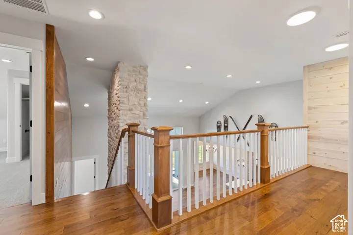 Upper level hallway featuring hardwood flooring, horizontal wood-plank accent walls, and a wood and white spindle railing