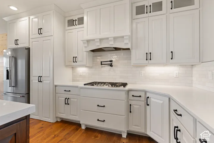 Kitchen featuring custom white cabinetry with glass-front uppers, light quartz countertops, subway tile backsplash, built-in gas cooktop with a wall-mounted pot filler, and hardwood flooring