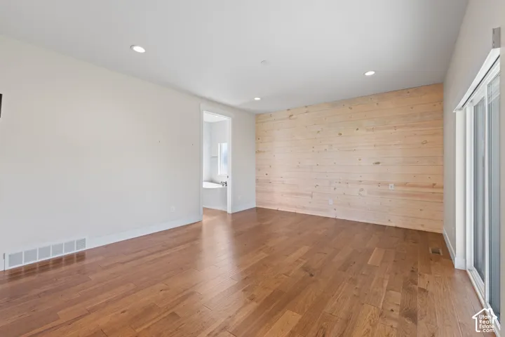 Primary bedroom featuring hardwood flooring, a horizontal wood-plank accent wall, recessed lighting, and a sliding glass door