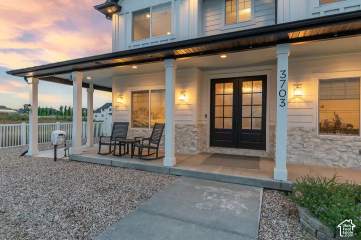 Exterior facade featuring white horizontal siding, stone masonry, covered front porch, double glass-paneled entry doors, and recessed ceiling lighting