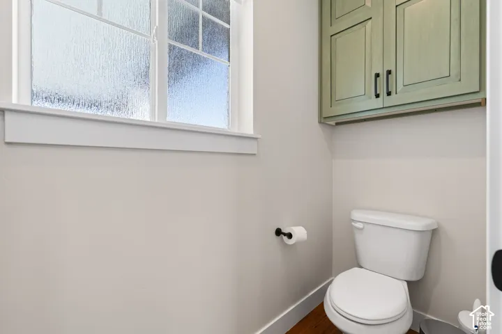 Water closet featuring privacy glass window, custom sage green wall-mounted cabinetry with matte black hardware, white porcelain toilet, and hardwood flooring