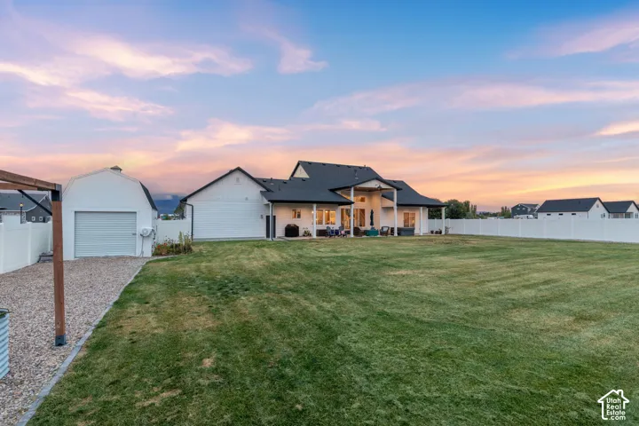 Expansive backyard featuring a large grass lawn, a detached storage building with a roll-up door, a covered patio, and perimeter vinyl fencing