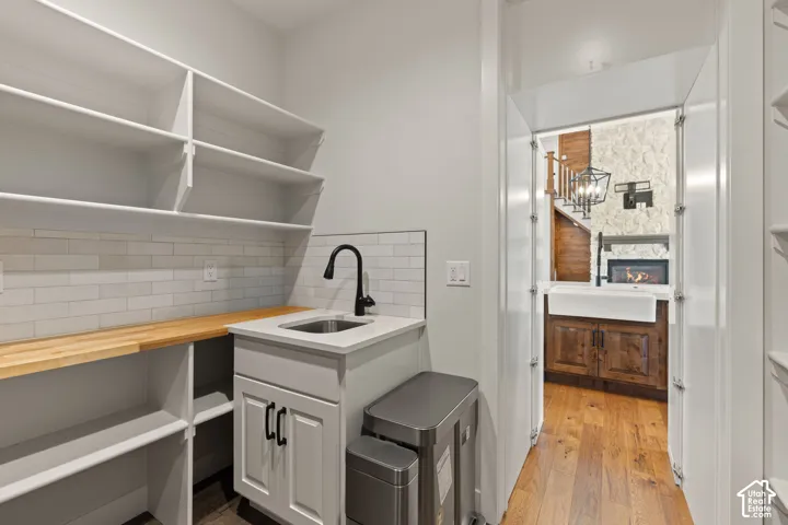 Walk-in pantry featuring custom white built-in shelving, wood-finish countertops, matte black plumbing fixtures, and a subway tile backsplash