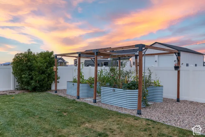 Backyard garden featuring corrugated metal raised beds, a wooden post trellis, crushed stone ground cover, and full-height vinyl fencing