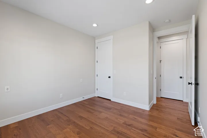 Main floor bedroom featuring hardwood flooring, neutral wall tones, recessed lighting, and white shaker-style interior doors with matte black hardware