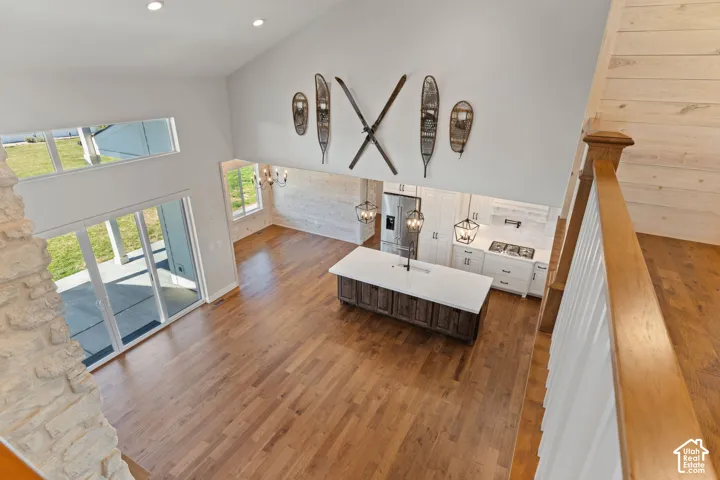 Vaulted ceilings with recessed lighting, stone-faced fireplace surround, hardwood flooring, center island featuring a white quartz countertop, expansive windows and glass sliding doors