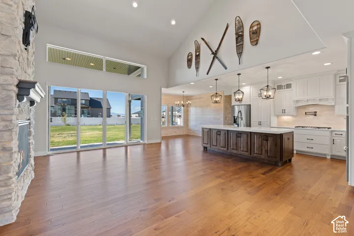 Vaulted ceiling with recessed lighting, full-height stone-clad fireplace, floor-to-ceiling sliding glass doors, kitchen island with dark wood-finish cabinetry, and hardwood flooring throughout