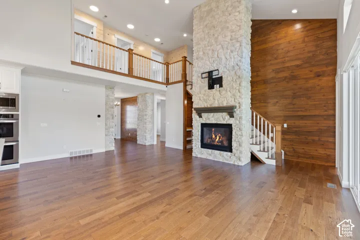 Two-story interior featuring hardwood flooring, a floor-to-ceiling stone fireplace, wood-paneled accent wall, and a mezzanine with white balustrade railing