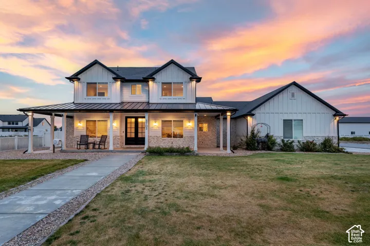 Modern farmhouse exterior featuring vertical board-and-batten siding, stone masonry, a metal roof covering the covered porch, and columns supporting the front overhang