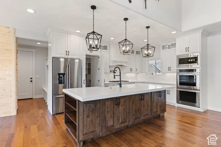 Kitchen featuring white upper cabinetry, a wood-finish island with quartz countertops, stainless steel built-in appliances, pendant lighting, and hardwood flooring