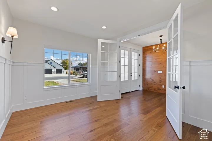 Hardwood flooring, white board-and-batten wainscoting, French doors with glass panes, wood-plank accent wall, and recessed lighting