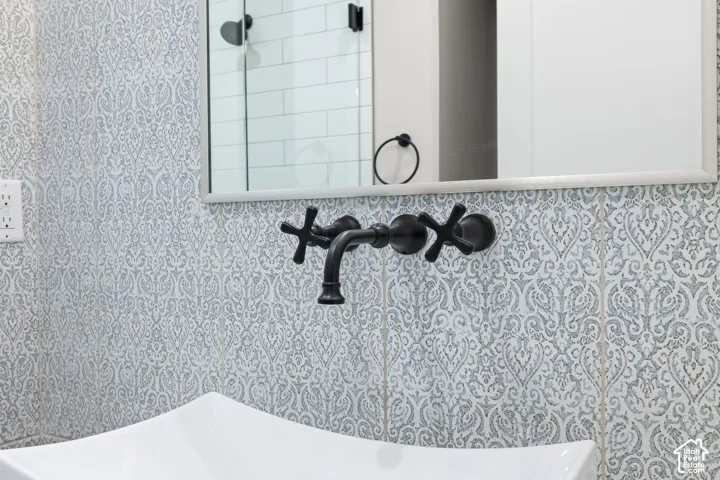 Main floor bathroom featuring vessel sink with a wall-mounted matte black faucet with cross handles, set against patterned tile wall, and paired with a rectangular mirror