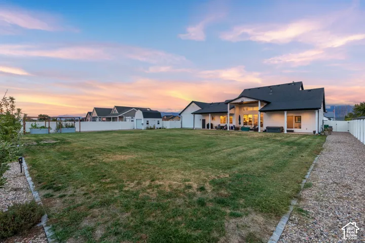 Expansive backyard featuring a large grass lawn, a covered patio with recessed lighting, perimeter vinyl fencing, a detached garage, and raised garden beds