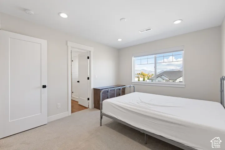Neutral-toned bedroom featuring recessed lighting, carpeting, solid-core interior doors with matte black hardware, and a single-hung window with mountain scenery, plus access to an ensuite bathroom