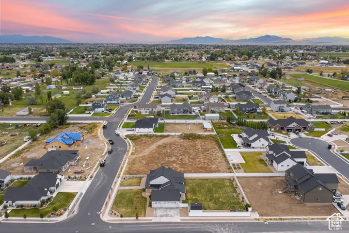 Aerial perspective of a residential corner lot featuring a multi-car garage, concrete driveway, established lawn, and mountain skyline backdrop